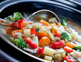 Close-up of a ladle and a slow cooker full of stew.