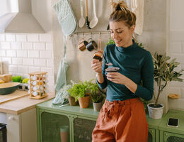 A woman leans on her kitchen counter as she eats yogurt.