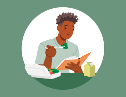   A man eating a salad and reading a book.