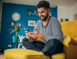 A man sits cross-legged and smiles down at his phone.