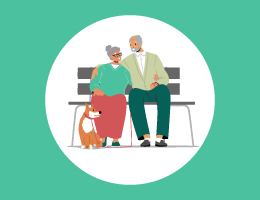 An elderly couple, smiling at each other, sit on a park bench with a dog at their feet.