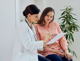 A doctor sitting next to a patient points something out on a piece of paper.
