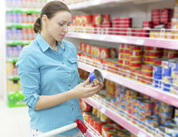 A woman in a grocery store looks at a can of food.