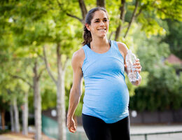 A pregnant woman carries a water bottle as she walks outdoors.