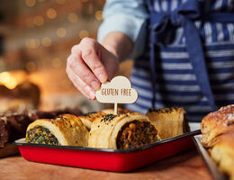 A hand places a "gluten-free" sign on a pastry in a bakery display tray.