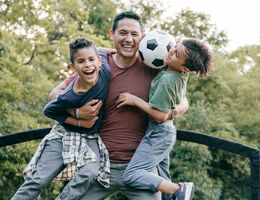 A dad laughs while playing outside with two laughing kids.