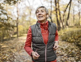 A woman jogs down a wooded path in autumn.